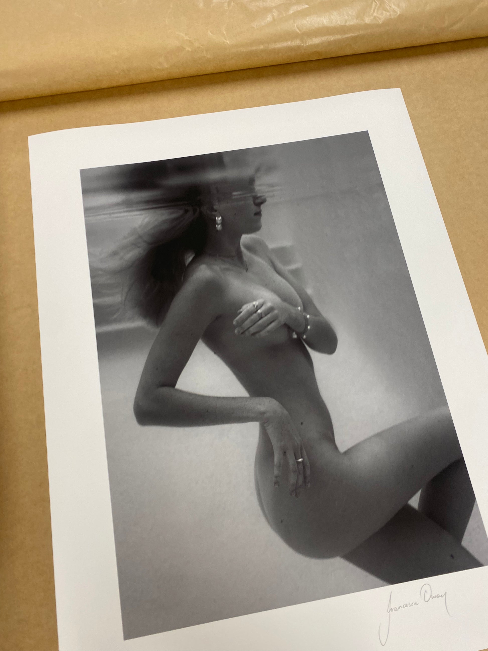 Unveiled 02" by Francesca Owen captures the allure of a nude subject submerged underwater with their face partially visible. The long hair floats ethereally in the water, and the subject is adorned with earrings. This black-and-white photograph, rendered using archival pigments, is printed on fine art paper to ensure its exquisite detail and depth are meticulously preserved.