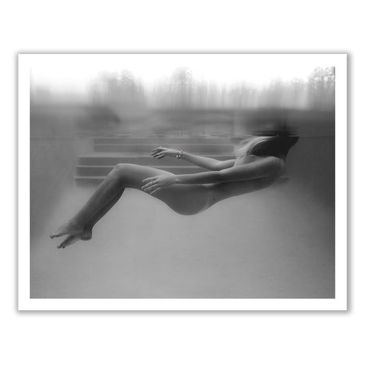Unveiled 04 by Francesca Owen is a black-and-white photograph capturing a person floating horizontally underwater with bent legs and relaxed arms. Set in a tranquil swimming pool, this serene image beautifully showcases the fluidity and calmness of being submerged. The photograph is printed on fine art paper using archival pigments, ensuring its longevity.