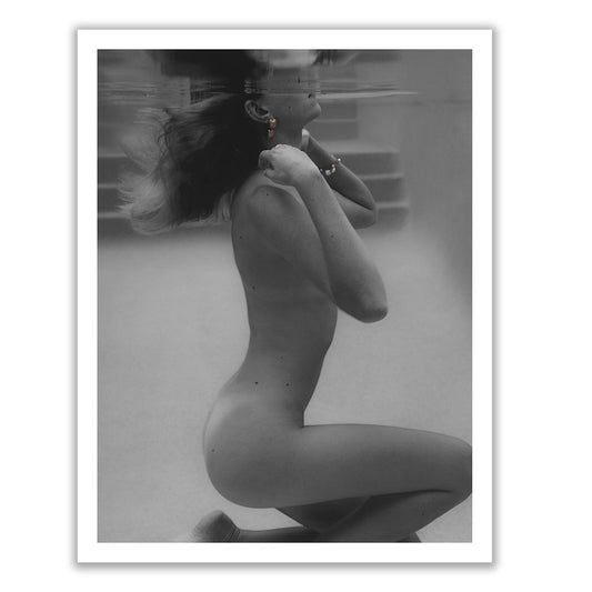 Two smiling individuals are holding a large framed black and white photograph from the "UNVEILED" collection by Francesca Owen. The fine art paper print features an artistic nude side profile of a person on their knees. The person on the left is wearing a floral dress, while the person on the right is in a white t-shirt and shorts.