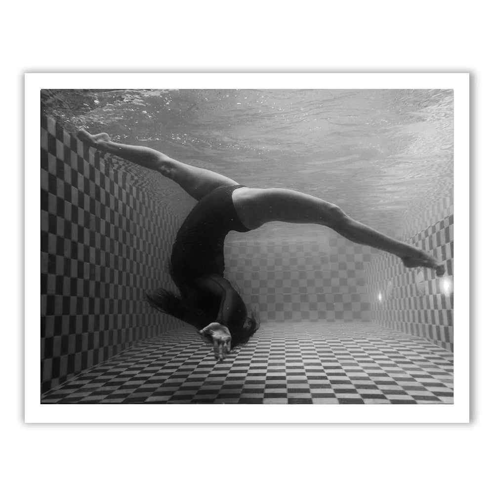 Immerse yourself in the surreal artistry of "Wild at Heart no.4 B&W" by Francesca Owen, capturing a mesmerizing black-and-white underwater photograph of a person in a black swimsuit performing an elegant backbend or contortion pose in an empty, checkered-tiled pool. The interplay of light and shadows adds to its artistic allure. Available on fine art paper with archival pigments, this piece can be custom-sized to perfectly complement any space.
